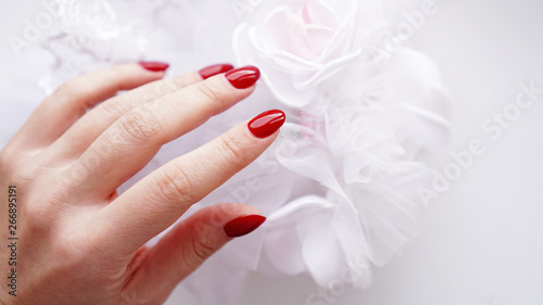 Beautiful female hand with red nails against the background of a white wedding bouquet
