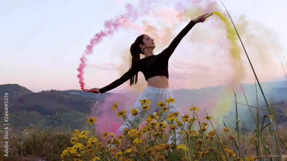 Bellissima ragazza felice, danza in una campagna con prato verde, con dei fumogeni colorati. Video al rallentatore.