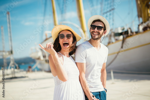 Happy young couple walking by the harbor of a touristic sea resort with sailboats on background © Mediteraneo