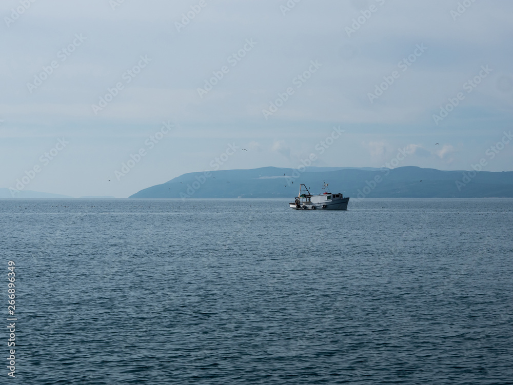 Small wooden fishing boat on calm sea with island at background