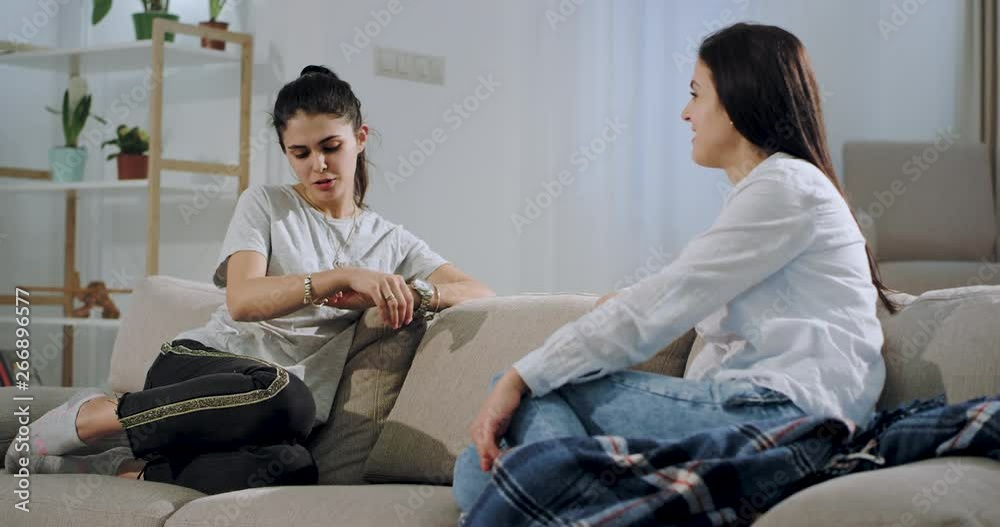 Two women friends smiling and chatting very friendly in the living room in the sofa , they spending a good time together. Two women friends smiling and chatting very friendly in the living room in the sofa , they spending a good time together.