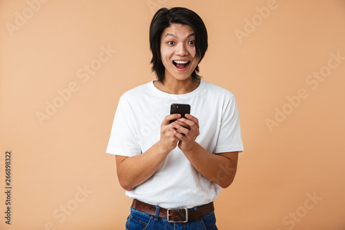 Photo closeup of asian guy 20s wearing white t-shirt laughing and holding cell phone photo