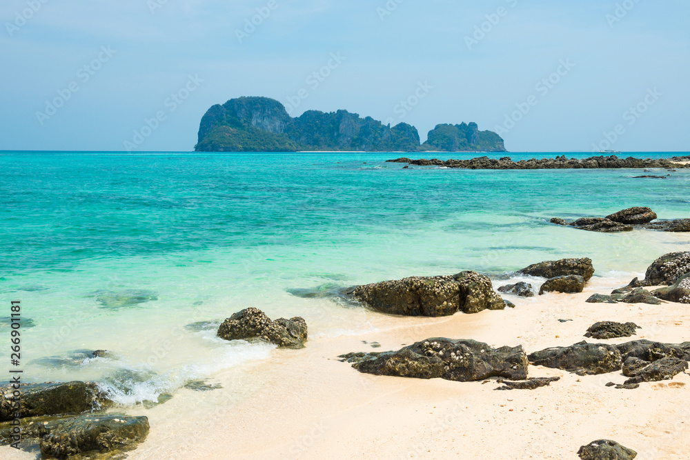 Tropical sea landscape with rocks at sand beach and rocky island at horizon