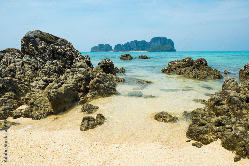 Tropical sea landscape with rocks at sand beach and rocky island at horizon Tropical sea landscape with rocks at sand beach and rocky island at horizon