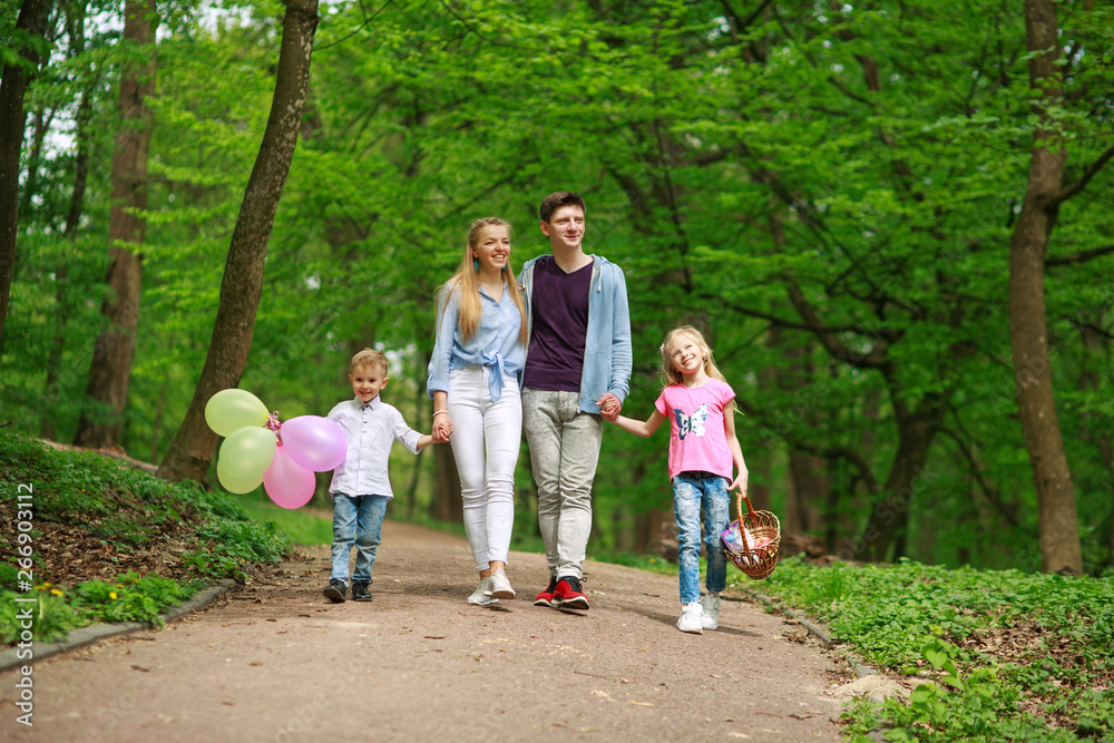 Family father and mother with two kids walking in summer green city park on picnic, happy holidays parents and children on nature Family father and mother with two kids walking in summer green city park on picnic, happy holidays parents and children on nature