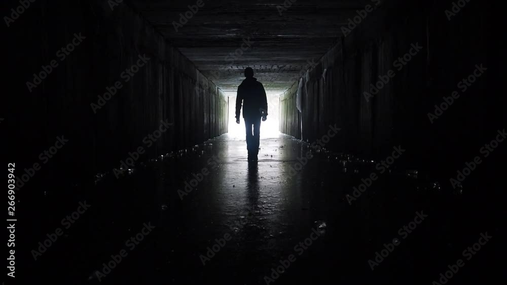 Man silhouette walking in a dark tunnel. Underground, post apocaloptic view. Exit concept. 