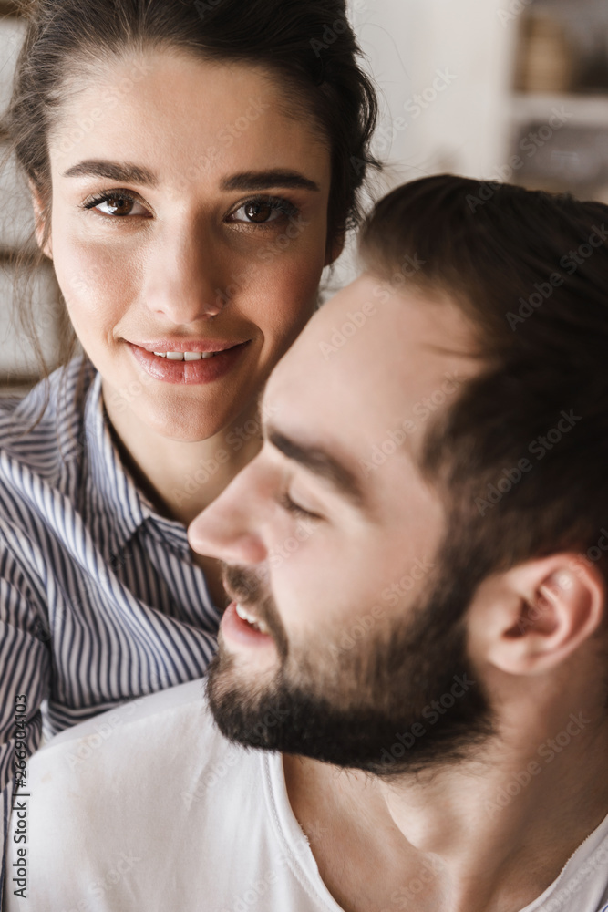 Image of lovely brunette couple smiling while hugging together at camera in apartment Image of lovely brunette couple smiling while hugging together at camera in apartment