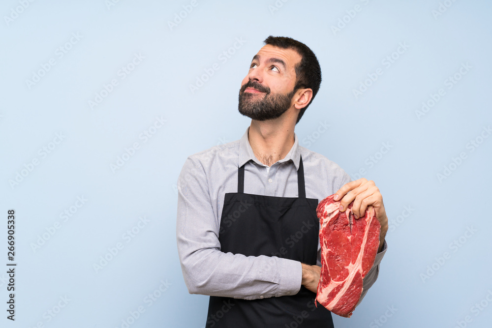 Chef holding a raw meat looking up while smiling Chef holding a raw meat looking up while smiling