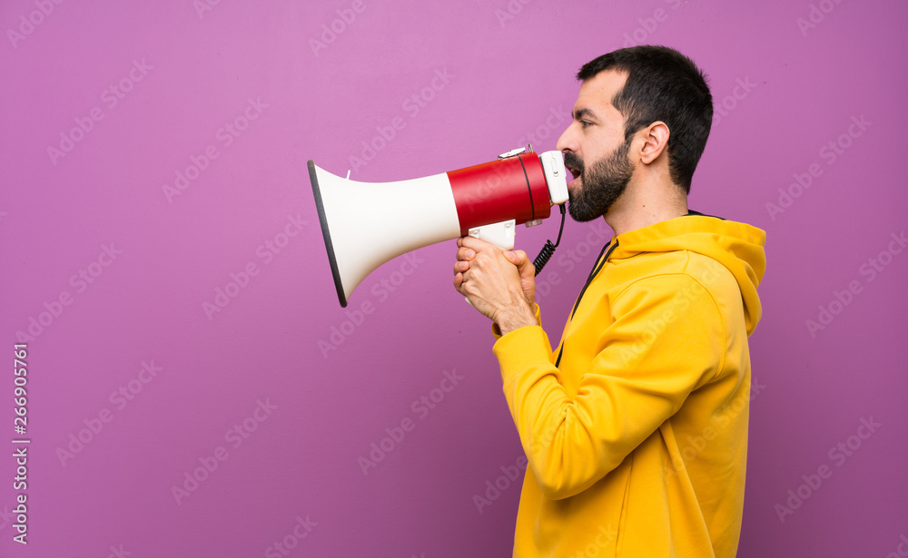 Handsome man with yellow sweatshirt shouting through a megaphone Handsome man with yellow sweatshirt shouting through a megaphone