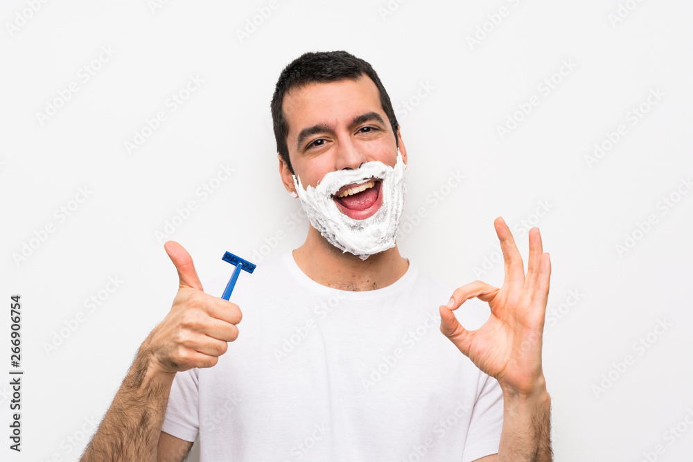 Man shaving his beard over isolated white background showing ok sign and thumb up gesture