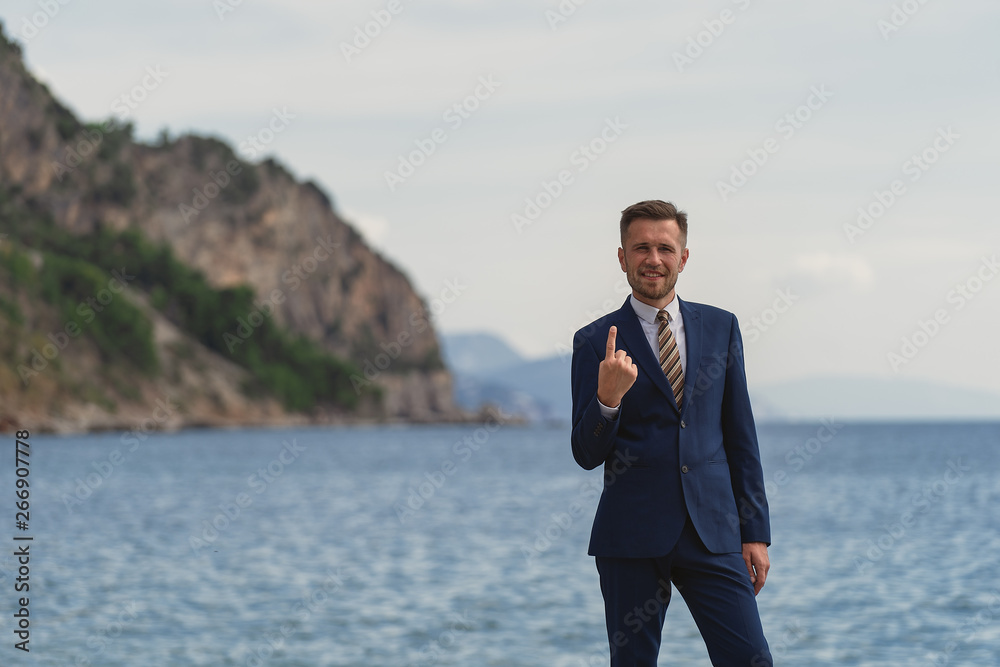 Businessman standing on the beach in a suit. Looks at camera and smiling showing gesture number one Businessman standing on the beach in a suit. Looks at camera and smiling showing gesture number one