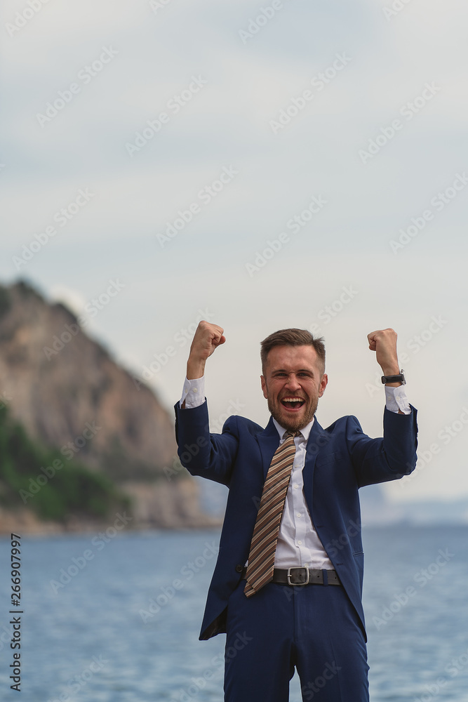 Excited businessman in a suit screaming and raising hands to the sky by the sea Excited businessman in a suit screaming and raising hands to the sky by the sea