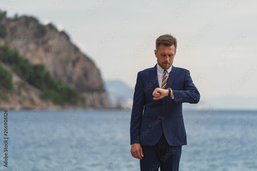 Businessman standing on the beach in a suit. Looks at the wristwatch Businessman standing on the beach in a suit. Looks at the wristwatch
