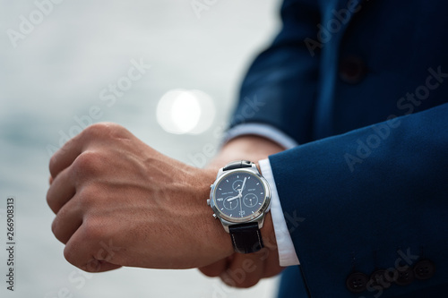 A man in a business suit checking a wrist watch on his hand on background  sea