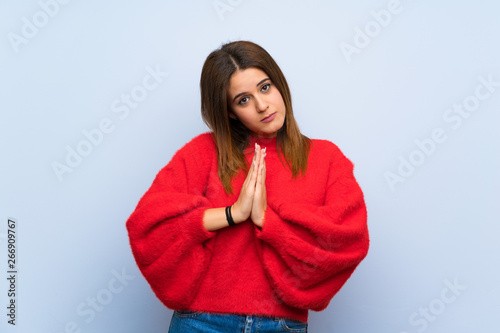 Young woman over isolated blue wall keeps palm together. Person asks for something © luismolinero