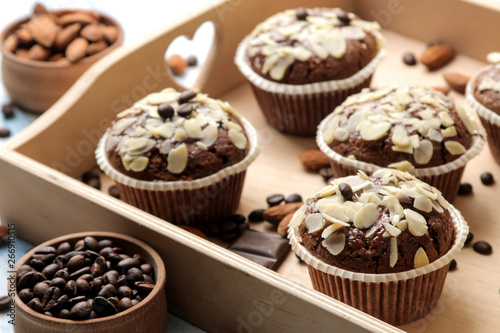 Delicious, sweet chocolate muffins, with almond petals in a wooden tray next to grains of coffee on a blue wooden table.