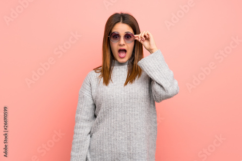 Young woman over pink wall with glasses and surprised