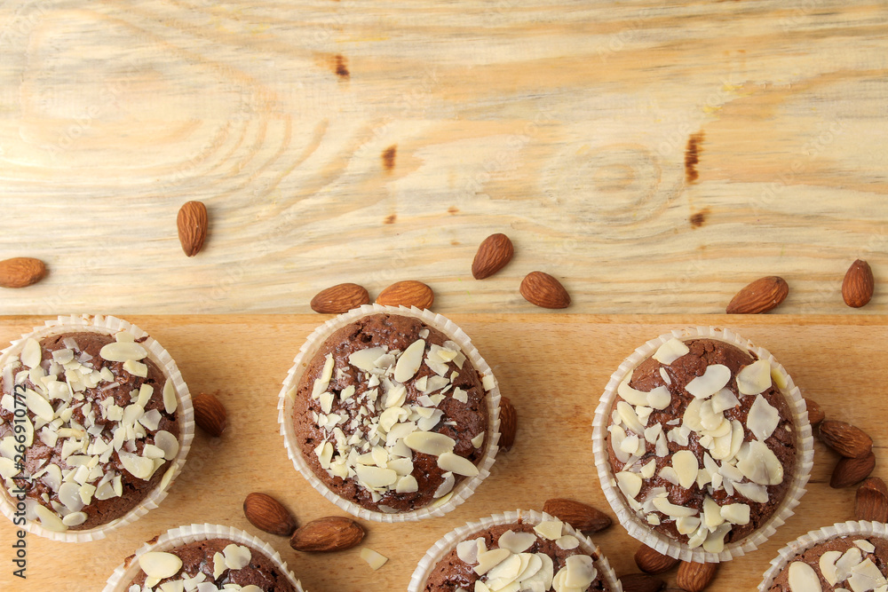 Delicious, sweet chocolate muffins, with almond petals next to almond nuts on a natural wooden table. top view Delicious, sweet chocolate muffins, with almond petals next to almond nuts on a natural wooden table. top view
