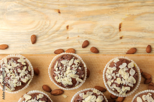 Delicious, sweet chocolate muffins, with almond petals next to almond nuts on a natural wooden table. top view