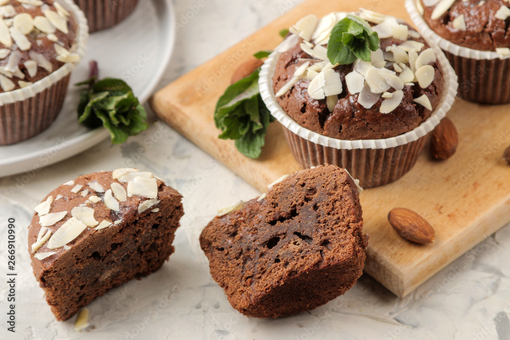 Delicious, sweet chocolate muffins, with almond petals next to mint and almond nuts on a light concrete table. close-up