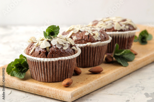 Fototapeta Naklejka Na Ścianę i Meble -  Delicious, sweet chocolate muffins, with almond petals next to mint and almond nuts on a light concrete table. close-up