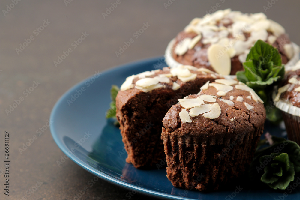 Delicious, sweet chocolate muffins, with almond petals next to mint and almond in a plate on a dark table.
