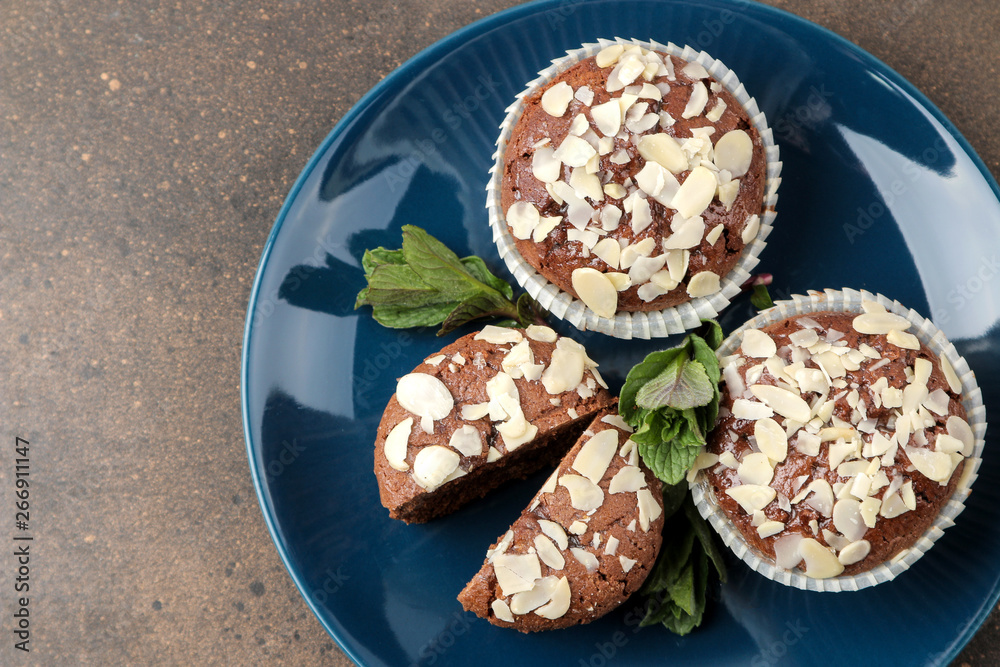 Delicious, sweet chocolate muffins, with almond petals next to mint and almond in a plate on a dark table. top view