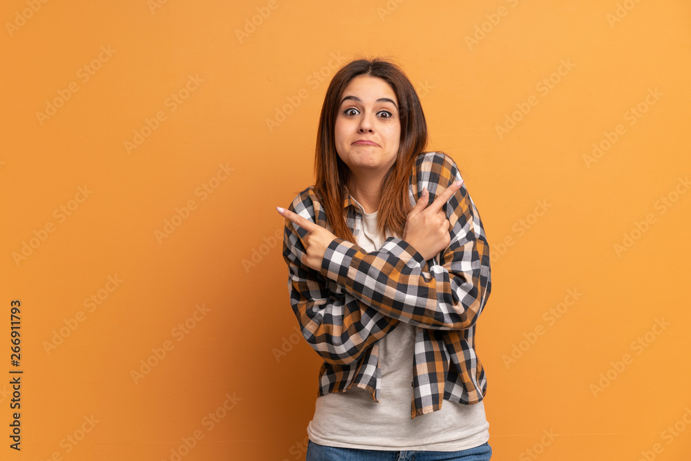 Young woman over brown wall pointing to the laterals having doubts Young woman over brown wall pointing to the laterals having doubts