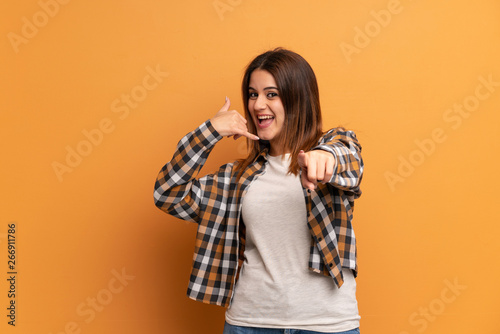 Young woman over brown wall making phone gesture and pointing front © luismolinero
