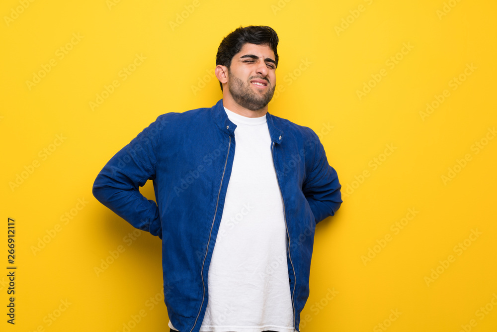 Man with blue jacket over yellow wall suffering from backache for having made an effort Man with blue jacket over yellow wall suffering from backache for having made an effort