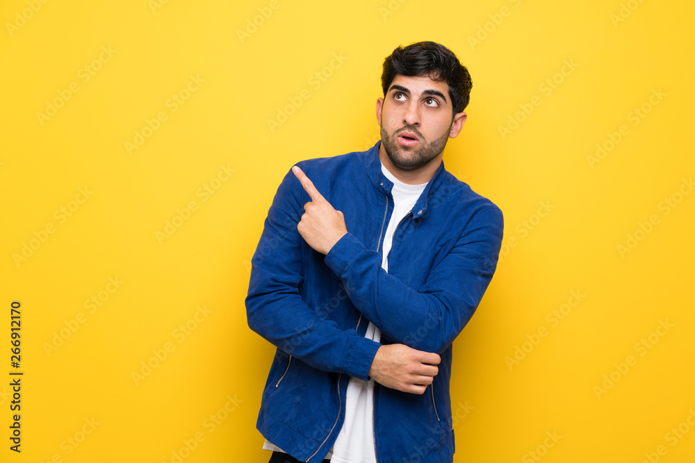 Fototapeta premium Man with blue jacket over yellow wall surprised and pointing side