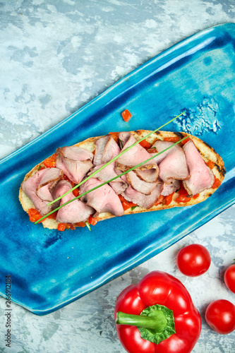 On a blue plate of bruschet with beef and tomatoes. Light gray textured background. Beautiful serving of dishes. Restaurant menu photo