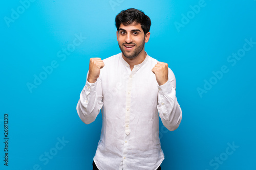 Young man over isolated blue wall celebrating a victory in winner position