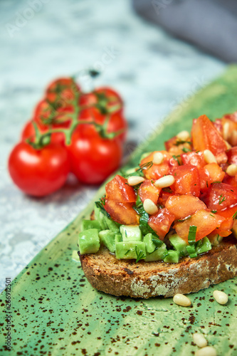 On a green plate of brusket with tomatoes and avocado. Light gray textured background. Beautiful serving of dishes. Restaurant menu photo