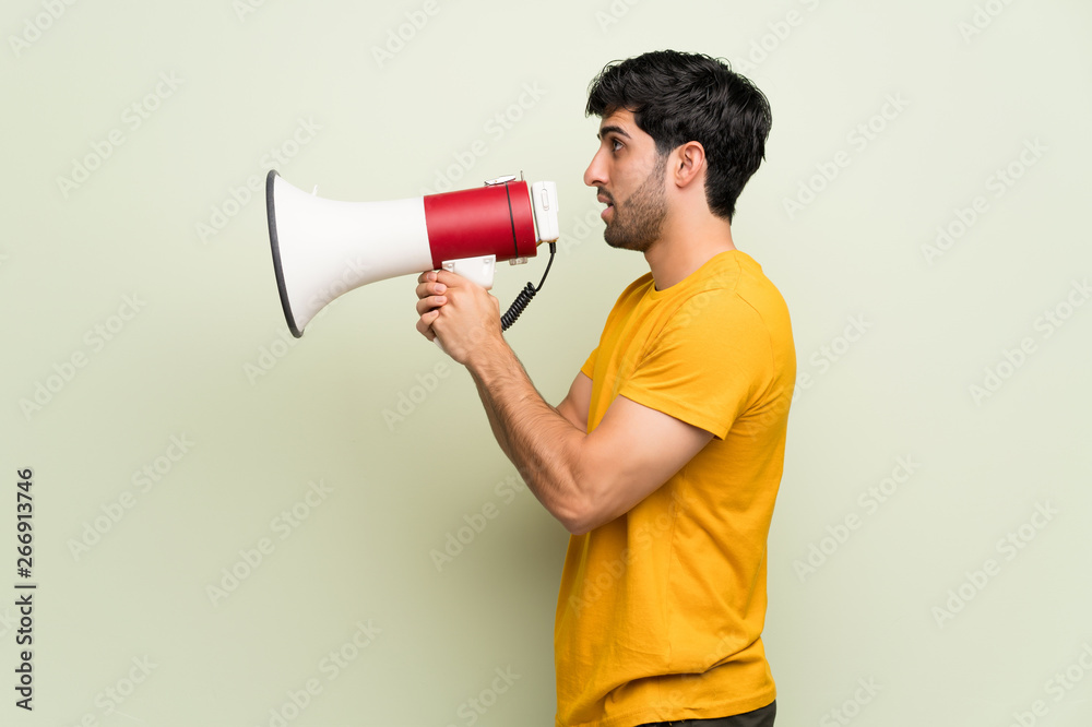 Young man over pink wall shouting through a megaphone Young man over pink wall shouting through a megaphone