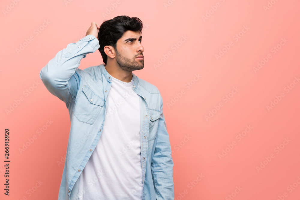 Young man over pink wall having doubts while scratching head
