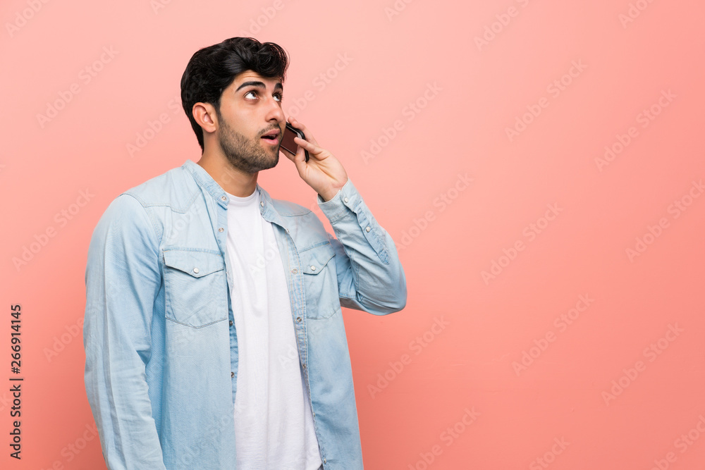 Young man over pink wall keeping a conversation with the mobile phone Young man over pink wall keeping a conversation with the mobile phone