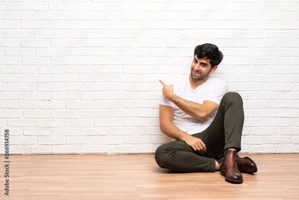Young man sitting on the floor pointing back Young man sitting on the floor pointing back