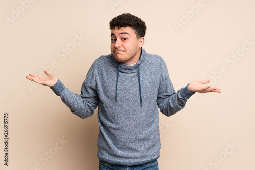 Young man over isolated wall making doubts gesture