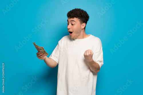 Young man over blue background taking a lot of money