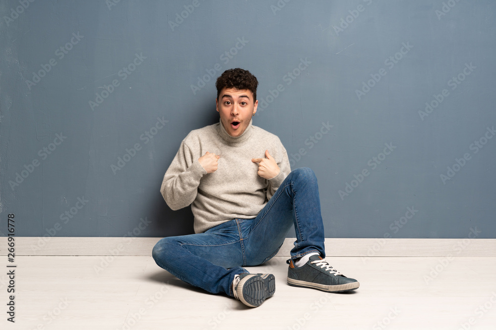 Young man sitting on the floor with surprise facial expression Young man sitting on the floor with surprise facial expression