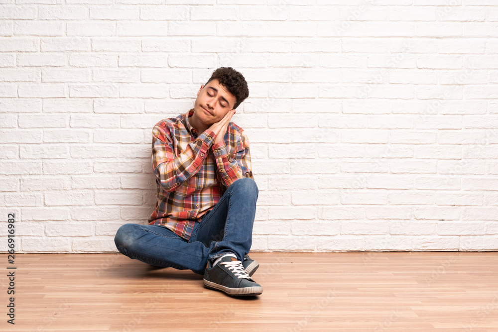 Young man sitting on the floor making sleep gesture in dorable expression Young man sitting on the floor making sleep gesture in dorable expression
