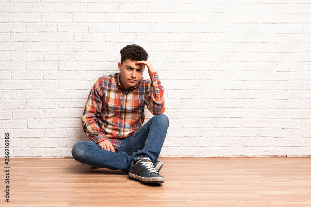 Young man sitting on the floor looking far away with hand to look something Young man sitting on the floor looking far away with hand to look something