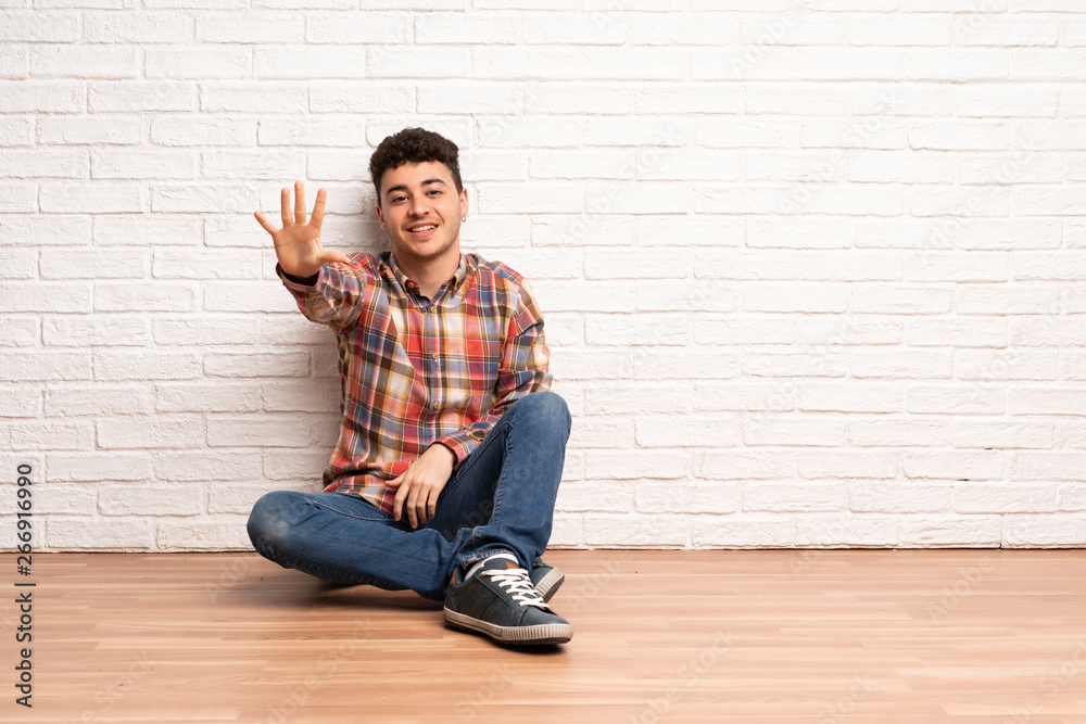 Young man sitting on the floor counting five with fingers Young man sitting on the floor counting five with fingers