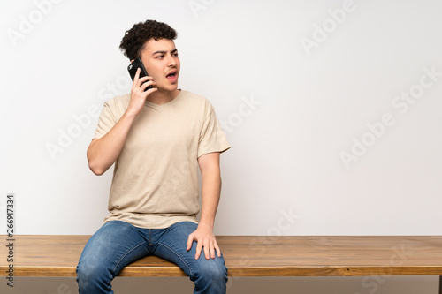 Young man sitting on table keeping a conversation with the mobile phone