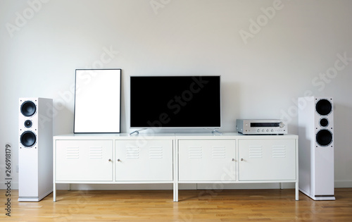 Poster on table in room.Modern audio stereo system with white speakers on bureau in modern interior