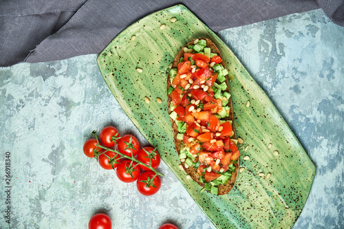 On a green plate of brusket with tomatoes and avocado. Light gray textured background. Beautiful serving of dishes. Restaurant menu photo