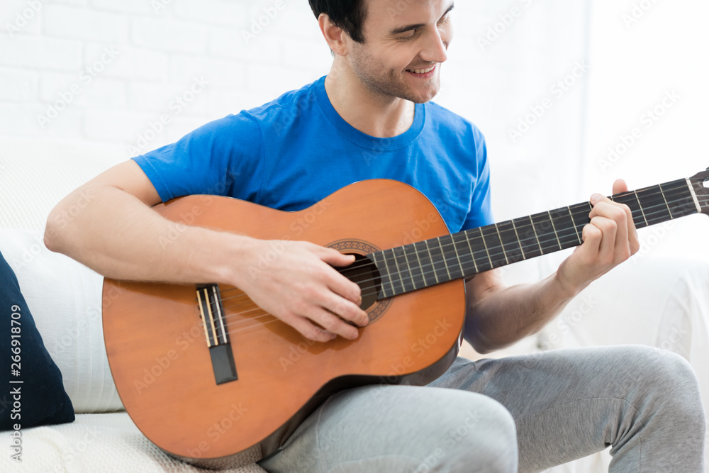 Handsome man playing on the guitar on the couch at home. Relaxed looking man sitting on a couch and playing the guitar. .
