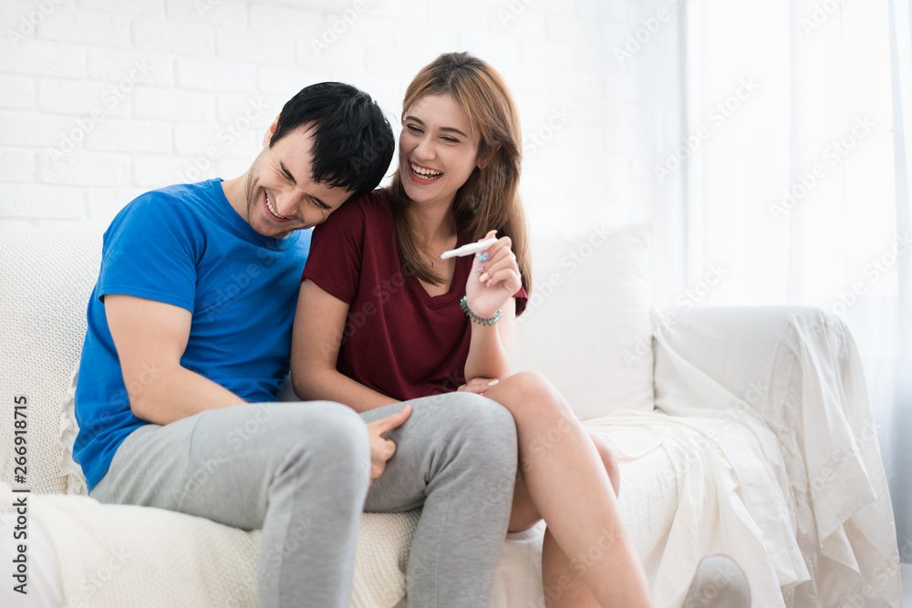 Closeup of happy young woman embracing man after positive pregnancy test sitting besides husband in room
