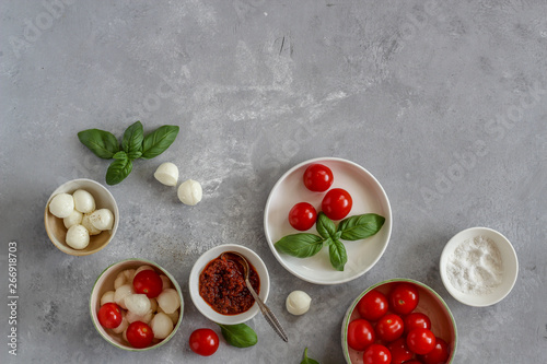 Small bowls with colorful ingredients of Caprese salad on a dark background with a copy space, flat lay style